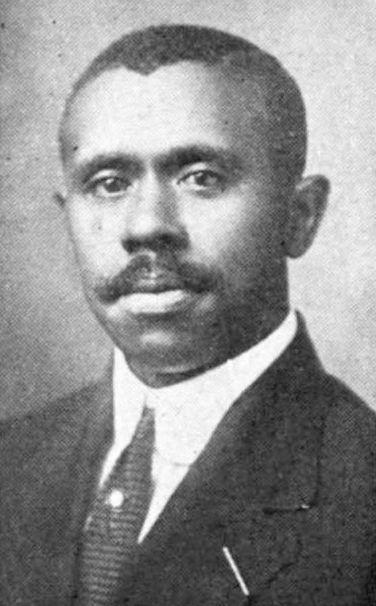 Whittico posing with in a suit accessorized with a lapel bar and tie pin